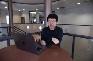 Xin Liang sitting at desk with laptop 